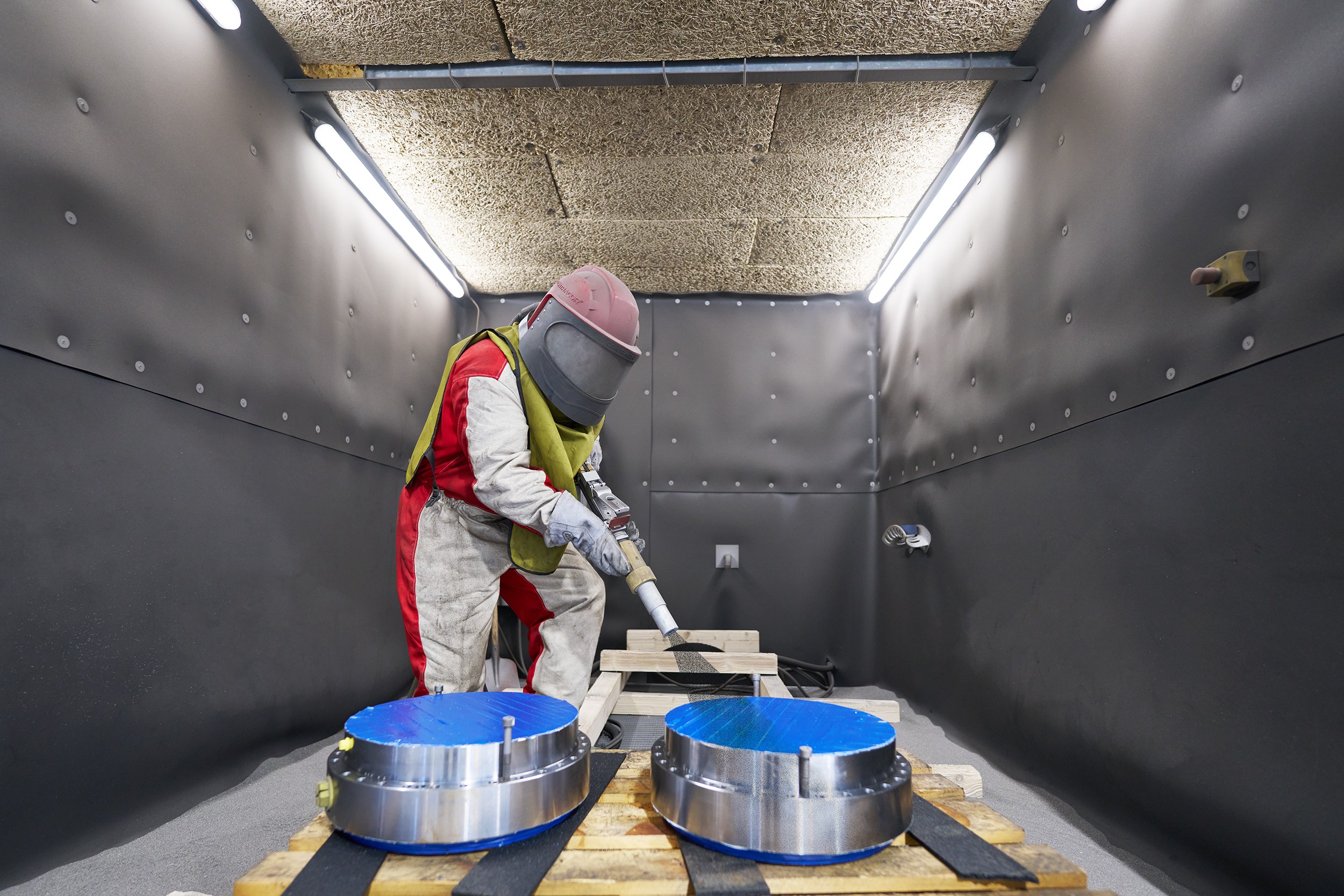 In einer Kabine bearbeitet ein Mitarbeiter Bestandteile von einem Hydraulikzylinder