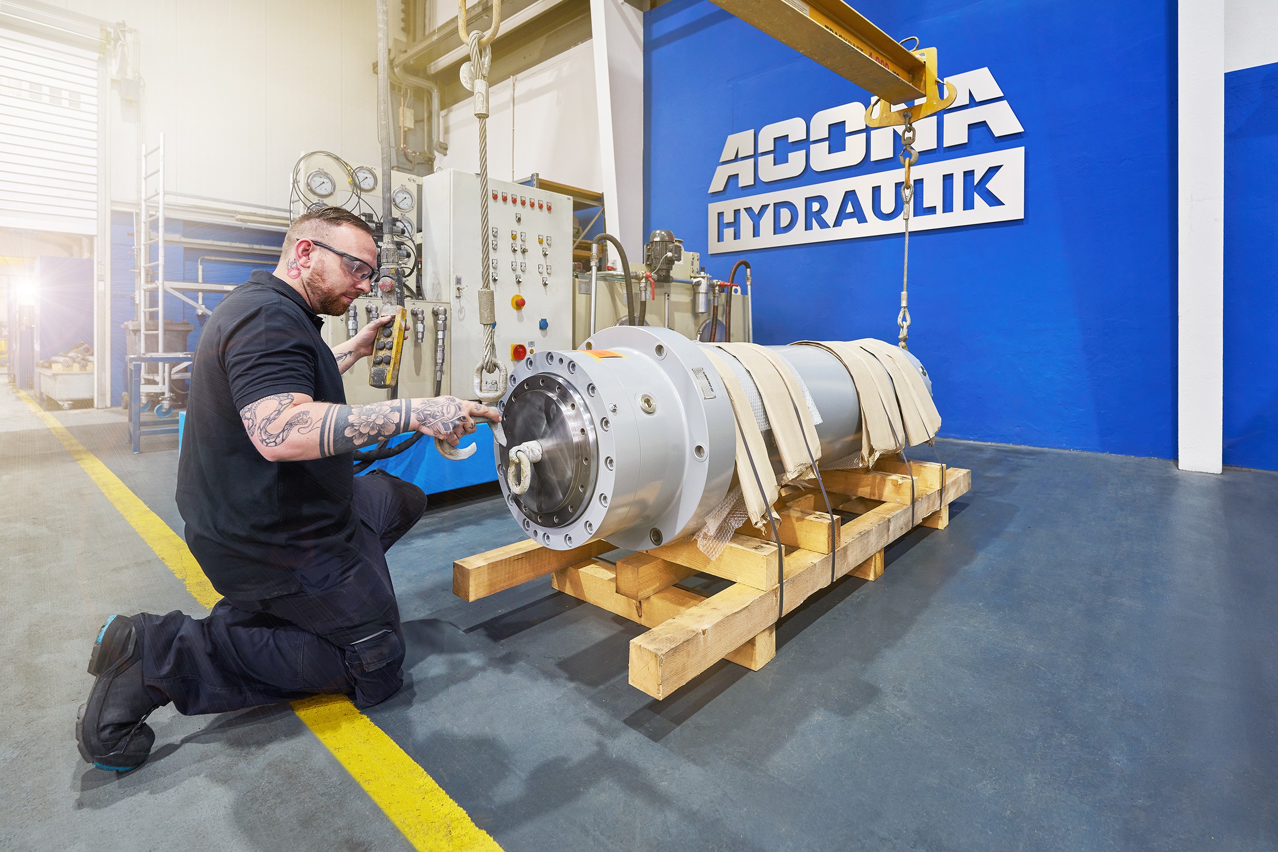 Ein Mitarbeiter von ACONA befestigt einen angelieferten Hydraulikzylinder an einem Kran